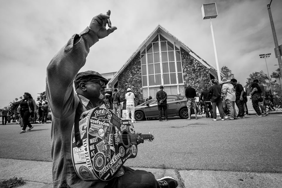 A man with a sticker-covered guitar raises his hand during a gathering outside a stone church in Oakwood